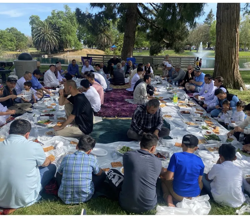 Families sharing a traditional meal on carpets in the park